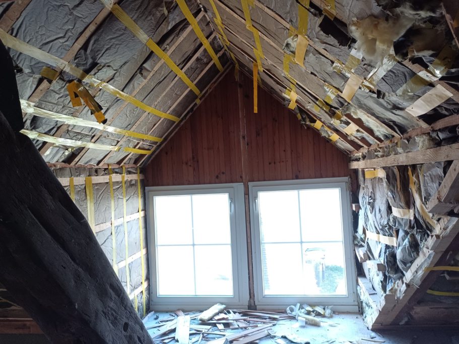 Intérieur d'un grenier avec des poutres apparentes et des murs non finis. Deux fenêtres visibles.