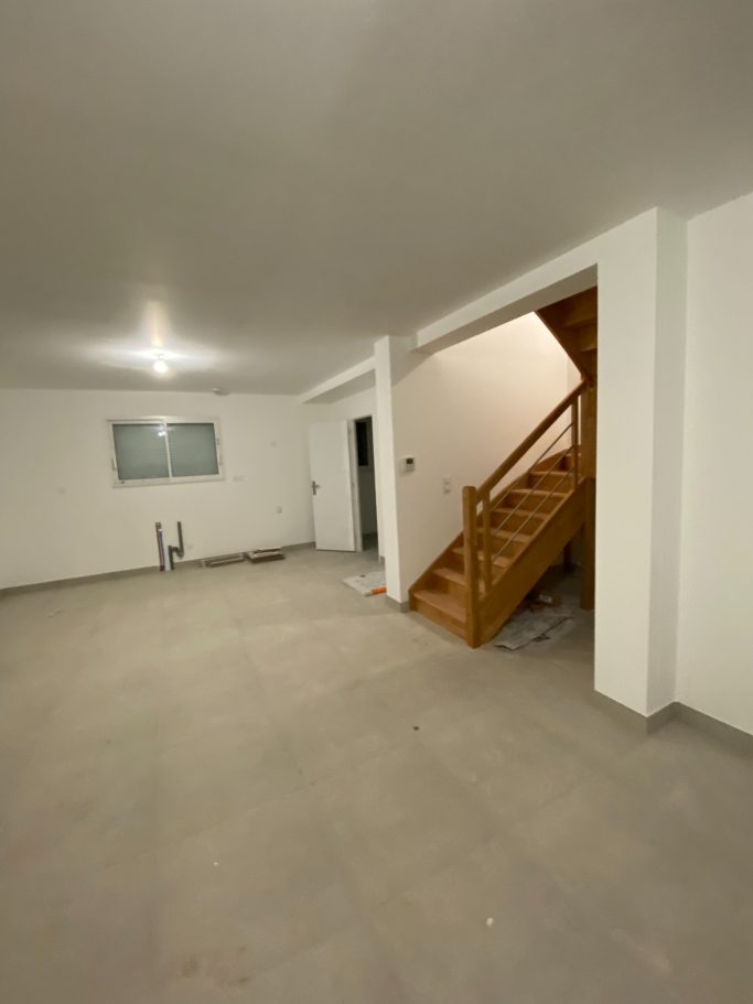 Intérieur d'un espace vide avec un escalier en bois et des murs blancs.